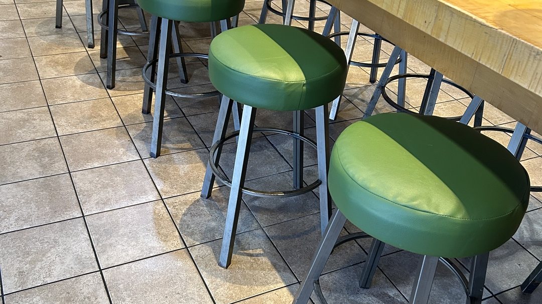 Row of Rubio's Coastal Grill bar stools reupholstered in two-tone green commercial vinyl along a butcher-block counter in San Diego